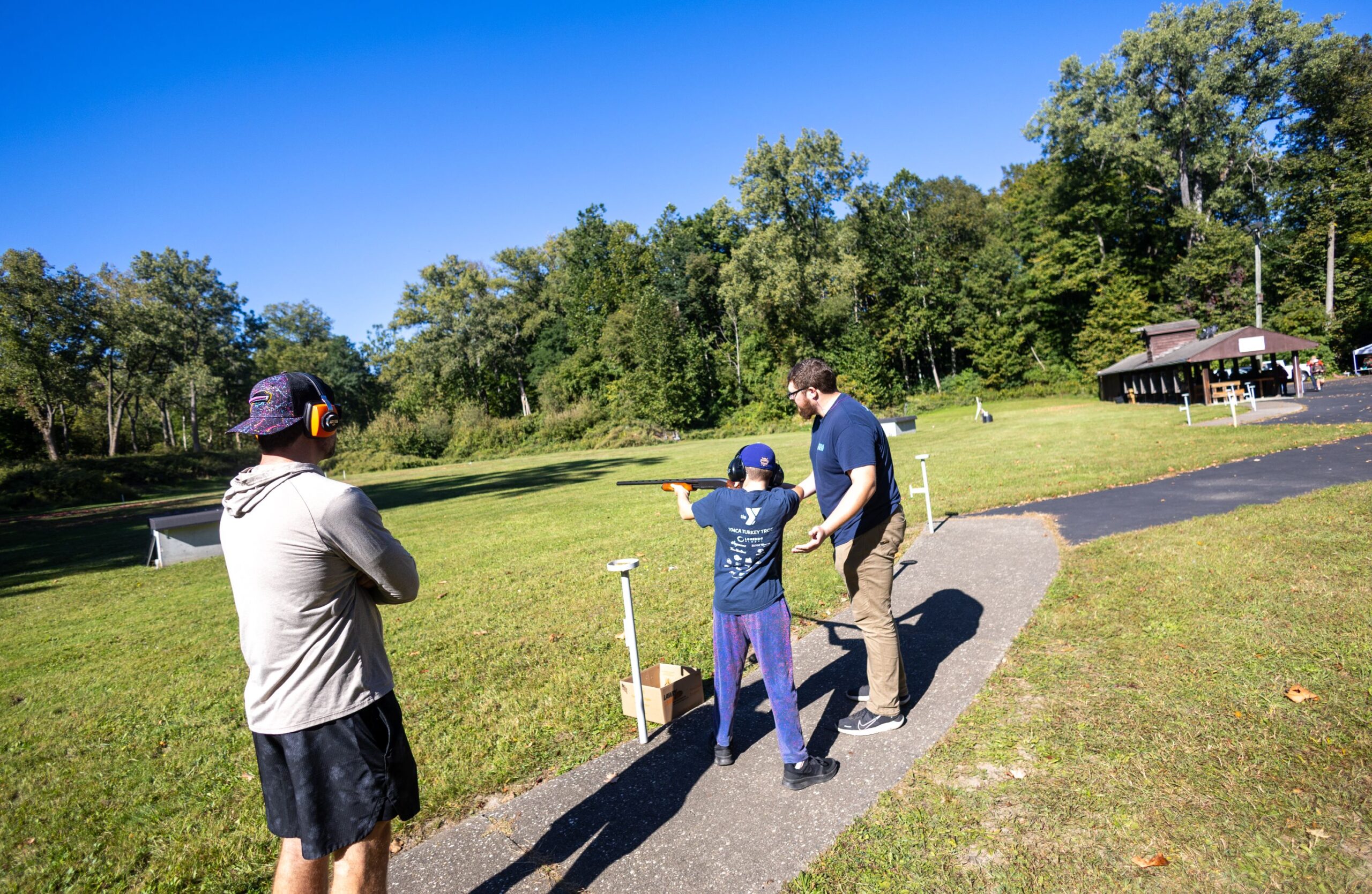 2026Sept26-048 Ryan M. getting trap instruction from a mentor with dad looking on.