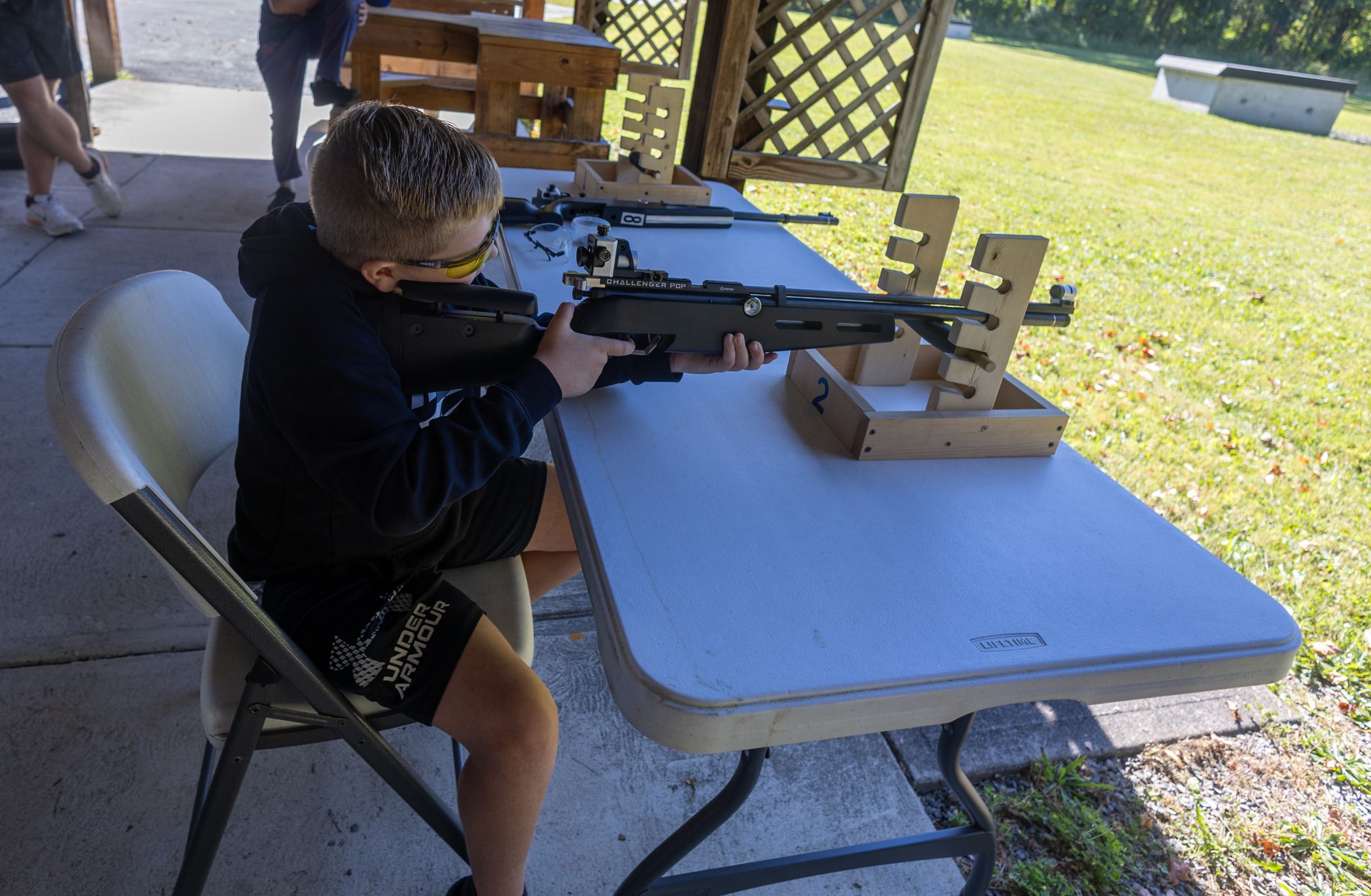 2026Sept26-055 Connor W. takes careful aim with an air rifle with his mentor watching.